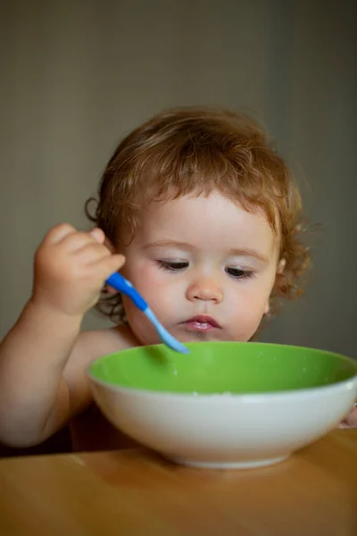 Concept de nutrition infantile. Bébé drôle manger de la nourriture lui-même avec une cuillère sur la cuisine. — Photo