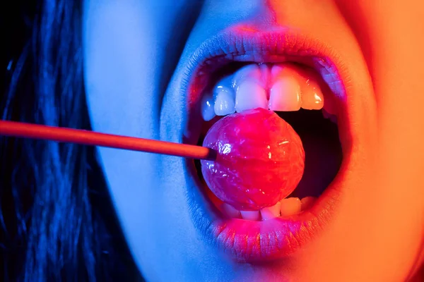 Close-up weibliche Lippen mit rosa Lipgloss hält im Mund rote Lutscher Bonbons. Lollipop Lippen Frauengesicht. — Stockfoto