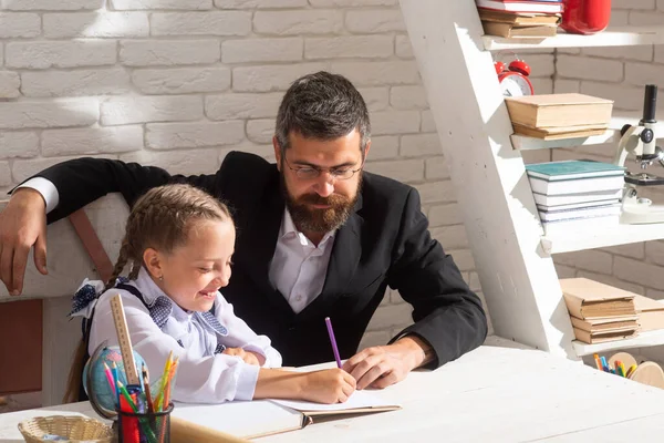 Elementär elev med lärare i klassrummet. Skolflicka studerar och skriver i klassrummet med lärare. Söt flicka studier med glad ansikte uttryck nära skrivbord med skolmaterial. — Stockfoto