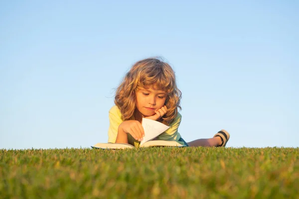 Έξυπνο παιδί ανάγνωση βιβλίο, που βρίσκεται στο γρασίδι στο πεδίο στον ουρανό και γρασίδι τομέα. Πορτρέτο των έξυπνων παιδιών. — Φωτογραφία Αρχείου