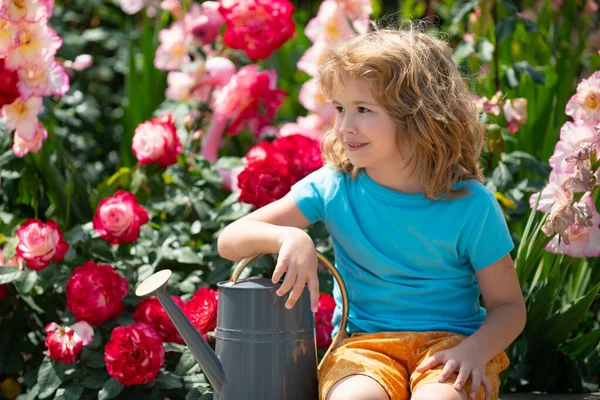 Милий кучерявий маленький хлопчик дитина в літній сукні, що працює в саду, поливаючи квіти. Діти садівництва. Діти працюють на задньому дворі. Малюк з водою може . — стокове фото