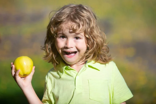 Retrato de menino segurando e comendo uma maçã sobre fundo natureza verde. — Fotografia de Stock