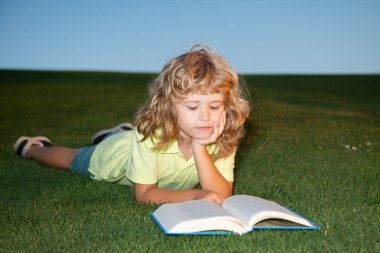 Elinde kitap olan okul çocuğu dışarıda dinleniyor. Bahçede kitabı olan çocuk. Çocuk yaz günü açık havada kitap okuyor..