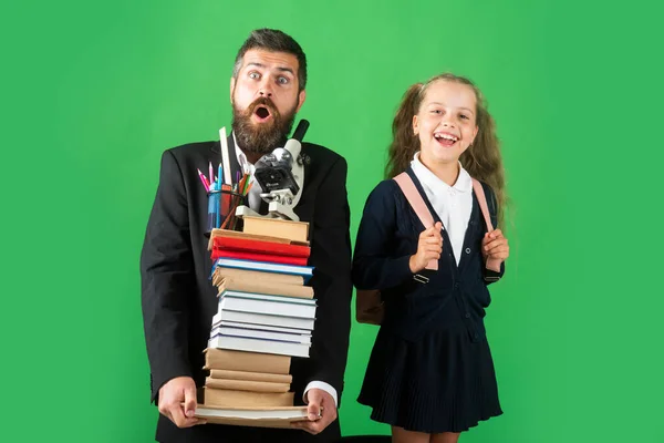 Grappige vader of leraar met schoolmeisje dochter houden grote stack school leerboek notebook boeken, geïsoleerd op groen. — Stockfoto