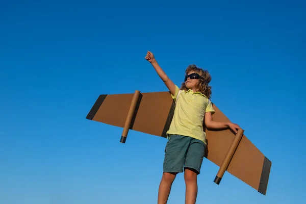 Niño piloto contra un cielo azul. Lindo chico soñador jugando con un avión de cartón. Infancia. Fantasía, imaginación. — Foto de Stock
