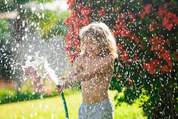 Los niños juegan con manguera de jardín de agua en el patio. Niños al aire libre diversión de verano. Niño jugando con manguera de agua en el patio trasero. Juego de fiesta para niños. Actividad saludable para un día soleado caluroso. —  Fotos de Stock