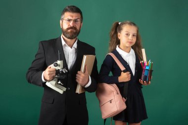 Ciddi bir öğretmen ve öğrencinin portresi okula hazır. Babamın portresi ve okul malzemeleriyle yeşil karatahta arka planda izole edilmiş küçük kızlar..