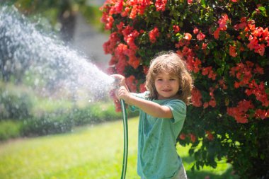 Küçük mutlu çocuk ev bahçesinde eğleniyor. Çocuk bahçe hortumunu tutuyor. Hasat zamanı arka bahçede çocuklar için açık hava oyunları.