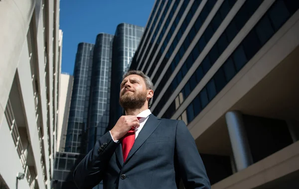 Biznesmen w niebieskim garniturze zawiązujący krawat na zewnątrz. Dobrze ubrany biznesmen w biurowcu miejskim. — Zdjęcie stockowe