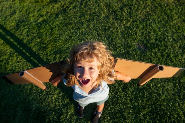 Enfant riant jouant avec des ailes d'avion jouet dans le parc d'été. Technologie d'innovation et concept de réussite. Enfant pilote s'amuser sur l'herbe dans le parc. — Photo