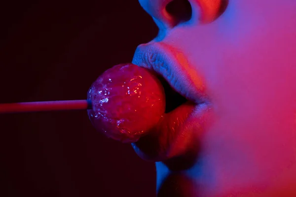 唇をしゃぶる。口の中でピンクのリップグロスを持つ女性の唇を閉じます赤いロリポップキャンディー。顔にロリポップ. — ストック写真
