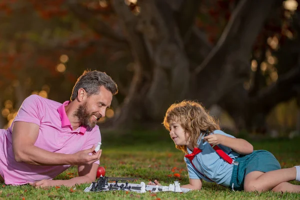 Otec a syn hrají šachy a tráví spolu čas v parku. Inteligentní dítě, chytré děti. — Stock fotografie
