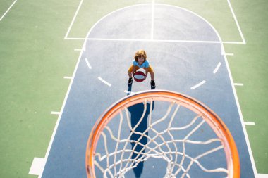 Oyun sahasında basketbol oynayan bir çocuğun üzerine açıyla bak..