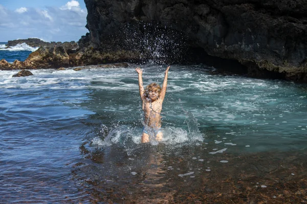 Bambino alza le mani in acqua e spruzza gocce d'acqua sul mare. Bambini vacanza estiva e concetto di viaggio. — Foto Stock