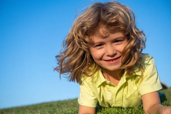 Een lachende jongen die geniet op het grasveld en droomt. Kinderen spelen op het zomerveld. — Stockfoto