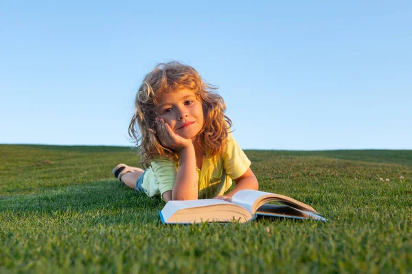 Söt unge läsa bok utanför i sommar park på gräs. — Stockfoto