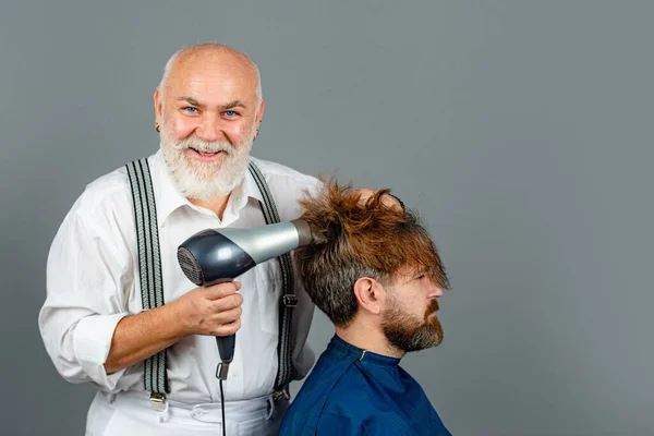 Berber dükkanında saç kurutma makinesiyle kuaförden saç stili alan sakallı adam. Elinde saç kurutma makinesi tutan mutlu kuaför.. — Stok fotoğraf