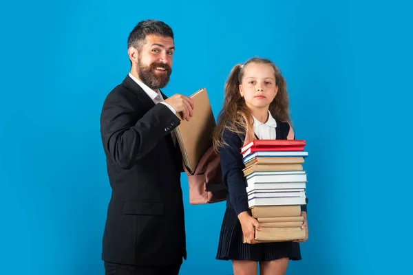 Schülerin mit einem Stapel Bücher, bereit für die Schule. Schwer zu studieren. Vater bereitet Rucksack mit Schulmaterial für Tochter vor. — Stockfoto