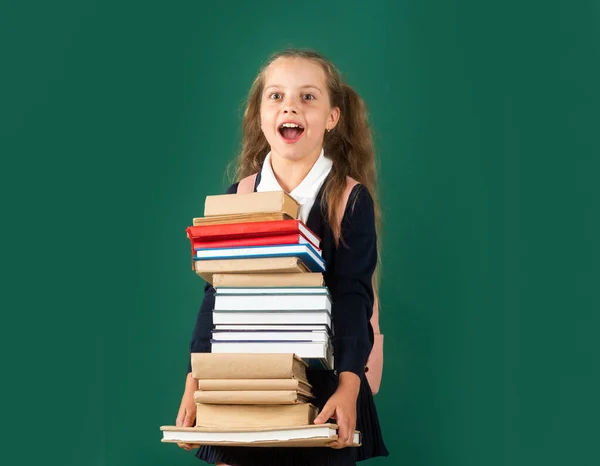 Kunskapsdag, leende rolig liten skolflicka med ryggsäck hålla böcker på grön svarta tavlan. Begreppet livsstil i barndomen. Utbildning i skolan. — Stockfoto