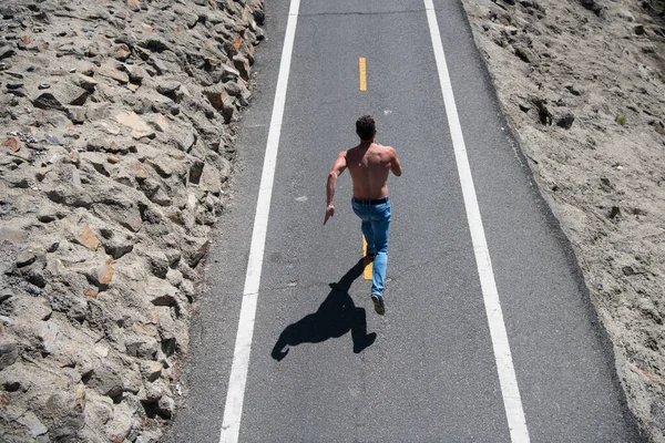 Achteraanzicht van atletische jongeman rennend met naakt bovenlijf. Sport- en fitnessloopster die op de weg traint voor marathonloop — Stockfoto