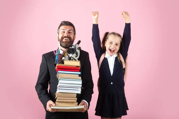 Padre o maestro tienen grandes cuadernos de libros de texto de la escuela de pila. Feliz niña preadolescente emocionada lleva uniforme escolar que sostiene la mochila aislada en rosa, retrato. —  Fotos de Stock