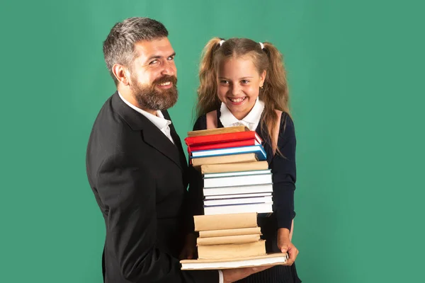 Vater führt seine Schülerin zur Schule. Porträt eines modernen Familienvaters und kleiner Mädchen isoliert auf einer grünen Tafel. Kleines Mädchen mit einem Stapel Bücher. Schwer zu studieren. — Stockfoto