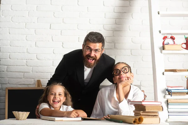 Porträt eines glücklichen Vaters und seiner Töchter in der Schule. Buch lesen und schreiben. Papa unterrichtet Schulmädchen im Klassenzimmer. — Stockfoto