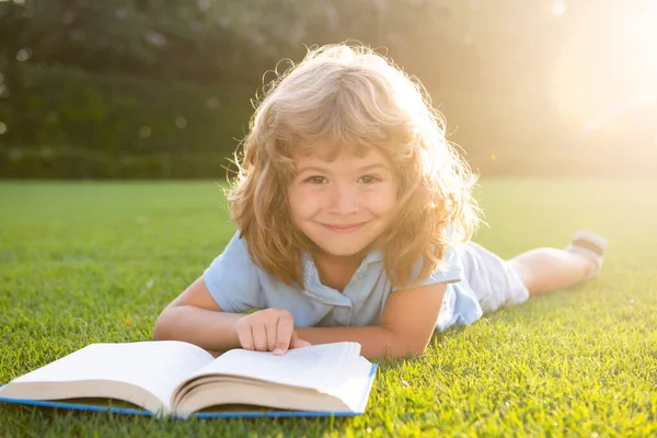 Een jongen die een interesseboek leest in de tuin. Zomertijd leuk. Leuke jongen liggend op het gras het lezen van een kids boek. — Stockfoto