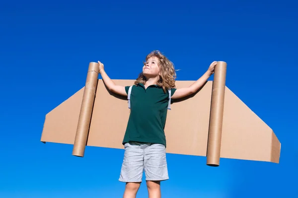 Criança feliz brincando com asas de brinquedo contra o fundo do céu de verão. Sucesso infantil, conceito de líder e vencedor. — Fotografia de Stock
