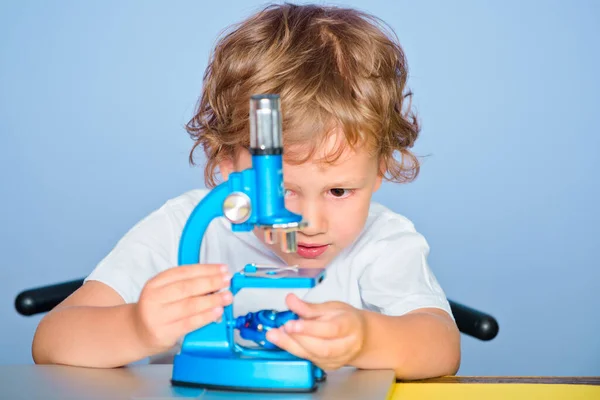 Aranyos kisfiú játszik mikroszkóppal. Az oktatás és az olvasás fogalma. — Stock Fotó