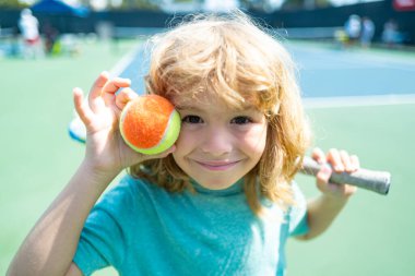 Tenis raketi ve topu dışarıda tenis kortunda olan bir çocuk. Çocuklar için spor egzersizi. Çocuklar için yaz etkinlikleri. Küçük çocuk için antrenman. Çocuk tenis oynamayı öğreniyor.