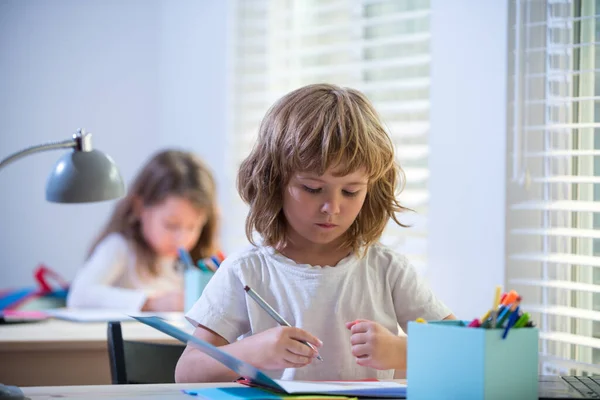 Escribir lindo alumno en el escritorio en el aula de la escuela primaria. Estudiante haciendo la prueba en la escuela primaria. Niños escribiendo notas en el aula durante la lección. — Foto de Stock