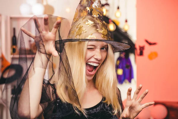 Belle femme surprise en chapeau et costume de sorcières montrant des produits. Portrait de femme Halloween. Sorcière d'Halloween avec une citrouille sculptée et des lumières magiques dans une pièce sombre. Concept de personnes d'Halloween. — Photo