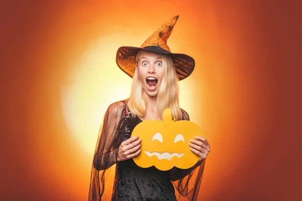 Décoration d'Halloween et concept effrayant. Joyeux gothique jeune femme en costume d'Halloween sorcière avec chapeau debout et souriant sur fond blanc. Sorcière d'Halloween avec citrouille. — Photo