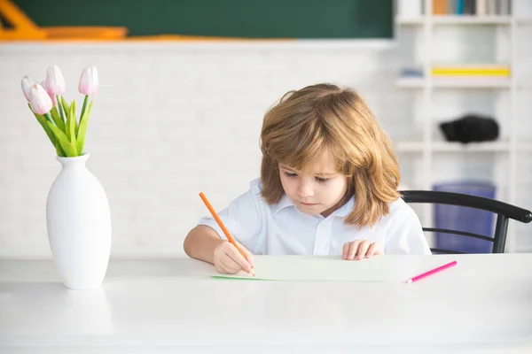 Crianças na escola, sala de aula. Menino da escola escrevendo em caderno e sentado à mesa em sala de aula. — Fotografia de Stock