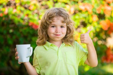 Tatlı çocuk dışarıda güneşli bir yaz sabahında çay ya da süt içmekten hoşlanıyor. Çocuklar açık havada sağlıklı dinlenme aktivitesi.