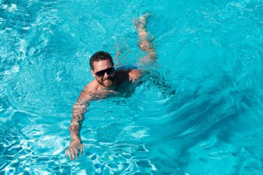 Yaz tatilindeki adam. Güneş gözlüklü adam havuzda yüzüyor. Yaz havuzu tatil köyü.