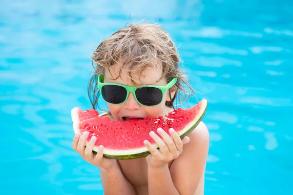 Niño con sandía sonriendo nadando en la piscina en verano en el complejo. Niños con trozo de sandía al aire libre. Vacaciones de verano y concepto de alimentación saludable. — Foto de Stock
