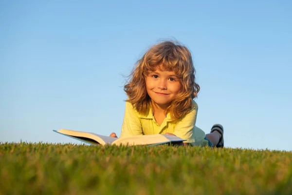 Boy child reading book, lying down on green grass. — Stock Photo, Image