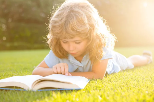 Netter Junge liest Buch auf grünem Gras. — Stockfoto