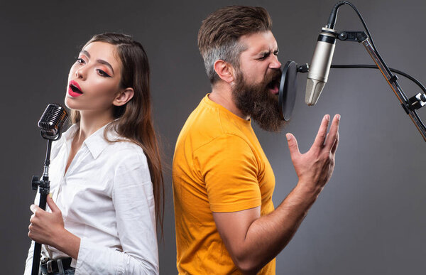 Singer duet couple is performing a song with a microphone while recording in a music studio.