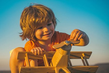 Çocuk seyahat etmeyi ve bir uçak pilotuyla oynamayı hayal ediyor. Mutlu çocuk mavi gökyüzü arka planında oyuncak uçakla oynuyor..