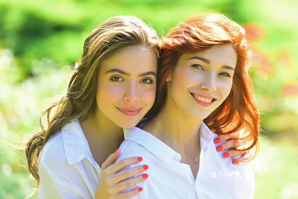 Två unga glada kvinnor vänner står i parken. Titta på kameran. Unga kvinnor i vit skjorta går på det gröna fältet. Bästa vänner. — Stockfoto