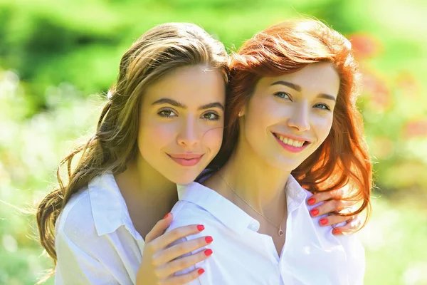 Duas jovens amigas felizes em pé no parque. a olhar para a câmara. Jovens mulheres de camisa branca estão andando no campo verde. Melhores amigos. — Fotografia de Stock