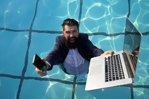 Funny bearded business man in suit using phone and laptop in swimming pool. Concept of young people working mobile devices. — Stock Photo, Image