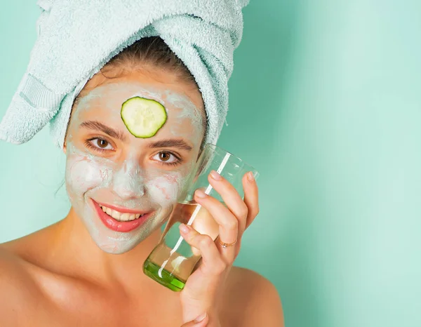 Happy smiling fresh looking young woman with a towel at her head and clay mud musk with cucumber do spa procedures. Daily skin care routine concept. — Stock Photo, Image