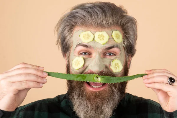 Kil maskeli, salatalık dilimli, yüzünde aloe vera bıyığı olan komik bir erkek model. Spa, cilt bakımı, sağlık ve yüz bakımı konsepti. Adamın kozmetik nemlendirici maskesi var.. — Stok fotoğraf