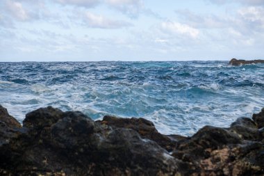 Deniz taşı plajı, deniz dalgaları. Renkli mavi deniz arka planı. Yaz tatili ve seyahat kavramı. Temiz deniz suyu, sahilde büyük taşlar..