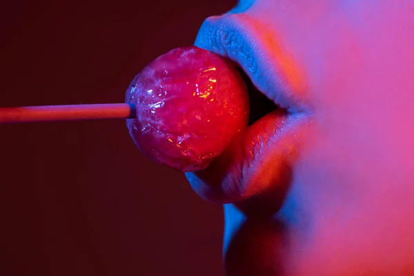 Labbra sessuali con caramelle, dolci sogni sexy. Sesso orale pompino concetto. La bocca femminile lecca chupa chups, succhia lecca lecca lecca. Luci al neon. Sfondo del night club. — Foto Stock