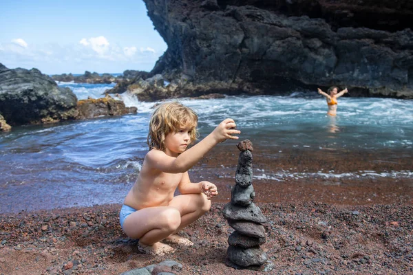 安定性、禅、調和、バランスを象徴する小石のビーチで石ピラミッドを作る面白い少年. — ストック写真